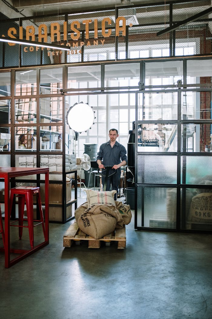 A worker in a coffee roastery warehouse transports coffee sacks on a trolley.
